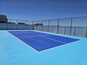 A newly installed pickleball court, built from the ground up. The court is light blue and Kansas City Blue with black vinyl fencing and sports court lighting.