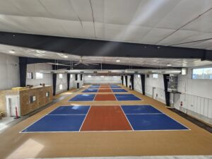 A set of 5 indoor pickleball courts with installed acrylic surfacing. Beige out of bounds, tournament blue in bounds and red in the kitchen.